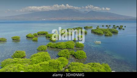 Gili Islands : vue aérienne petit bateau touristique naviguant sur une mer turquoise claire avec des îles vertes de mangrove entourées de zones coralliennes peu profondes. Chaîne de montagnes Lombok en arrière-plan. Voyage, aventure, explorer Banque D'Images