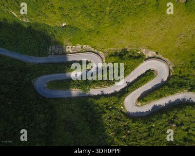 Vue aérienne d'une route serpentine serpente à travers les collines verdoyantes, un ruban de gris contre le paysage verdoyant, Dong Van, Hà Giang, Vietnam. Banque D'Images