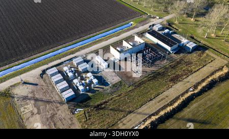 Vue aérienne d'une sous-station électrique avec des bâtiments blancs frappants contrastant avec la terre sombre et le canal bleu vif, Almere, pays-Bas. Banque D'Images