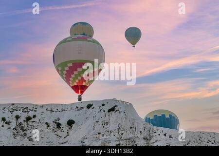 Des montgolfières volent près du soi-disant château de coton à Pamukkale, Türkiye, sur un lever de soleil coloré Banque D'Images