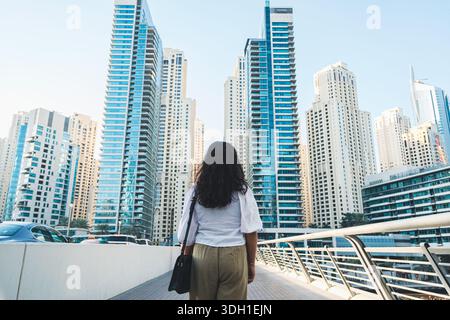 Bureau Going femme debout dans le quartier des affaires de Dubaï avec des tours de bureaux modernes, vue en angle bas Banque D'Images