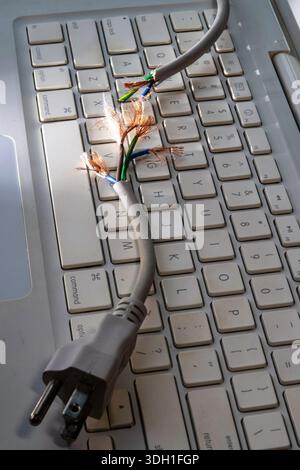Nature morte d'un cordon d'alimentation d'ordinateur effiloché sur un clavier d'ordinateur portable, 2026, États-Unis Banque D'Images