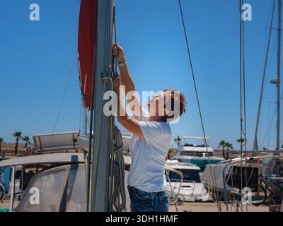 Femme marin tient le tissu de voile blanc se préparant à lever des voiles sur le yacht. L'activité physique et les compétences de manœuvre de bateau sont montrées pendant la préparation à l'as Banque D'Images
