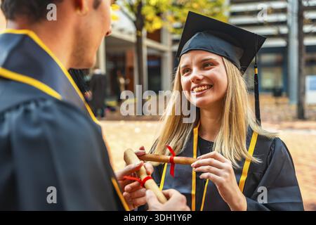 Diplômé universitaire souriant en casquette et robe accepte le diplôme roulé de la main invisible, célébrant la réussite scolaire, l'avenir brillant et fier milesto Banque D'Images