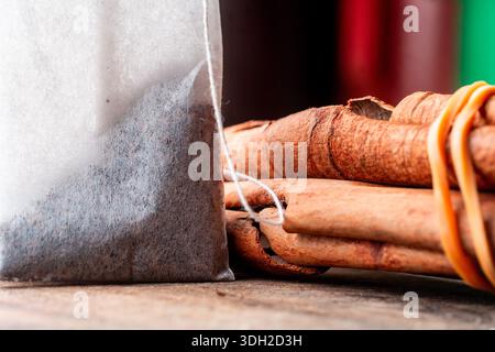 Plan macro d'un sachet de thé blanc reposant à côté de bâtonnets de cannelle séchés attachés avec une bande, placé sur une surface en bois rustique pour un thème de boisson chaude. Banque D'Images