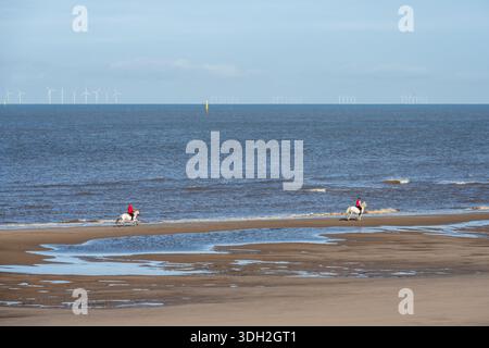 Les gens montent à cheval le long de Rossall Beach à Fleetwood, Lancashire, avec les parcs éoliens de la mer d'Irlande derrière. Banque D'Images