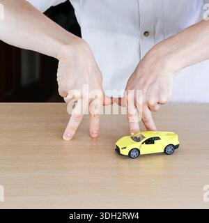 Paire de mains créant un cadre inversé par le dessus autour de la petite voiture de sport jouet jaune sur table en bois, concept de mise au point ou de protection Banque D'Images