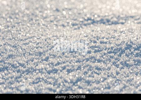Une vue rapprochée de cristaux de neige étincelants, légèrement éclairés par la lumière du soleil, créant un fond hivernal lumineux et texturé avec une atmosphère sereine et minimaliste Banque D'Images