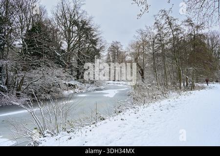 Une scène hivernale tranquille présente une rivière gelée bordée d'arbres luxuriants et enneigés. La lumière douce améliore l'atmosphère paisible, invitant la nature l Banque D'Images