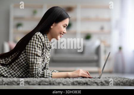 Vue latérale d'une jeune femme asiatique utilisant un ordinateur portable à la maison Banque D'Images