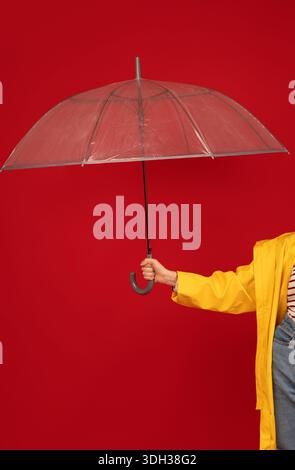 Femme en imperméable tenant un parapluie transparent contre le fond rouge, tir studio, recadrage. Concept d'accessoires d'automne Banque D'Images