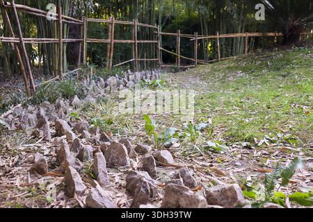 Ancienne lanterne en pierre debout dans un jardin japonais serein, entourée de clôtures en bambou, de rochers et de plantes vertes vibrantes sous une lumière douce. Banque D'Images