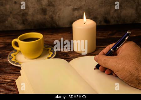 Gros plan d'une écriture à la main sur une page de carnet vierge avec du café et des chandelles sur du bois rustique. Concept de journalisation, de planification et de créativité. Banque D'Images