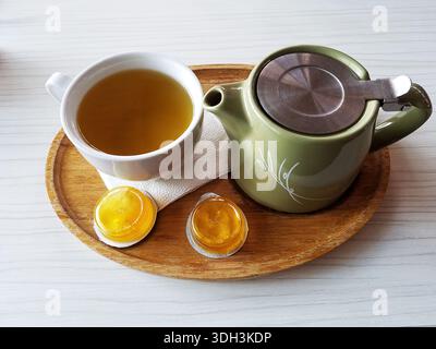 Un kit de service avec une bouilloire verte, du thé dans une tasse et deux gousses de miel. Banque D'Images