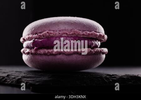 Macaron violet biscuits savoureux sur fond noir. Dessert traditionnel français, pâtisserie gourmande confiserie Banque D'Images