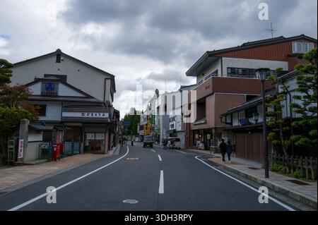Koya San, Japon - 21 octobre 2023 : une rue centrale de Koya San est bordée d'un mélange de bâtiments traditionnels et modernes, de boutiques, de panneaux de signalisation, de piétons et de véhicules sous un ciel nuageux. Banque D'Images