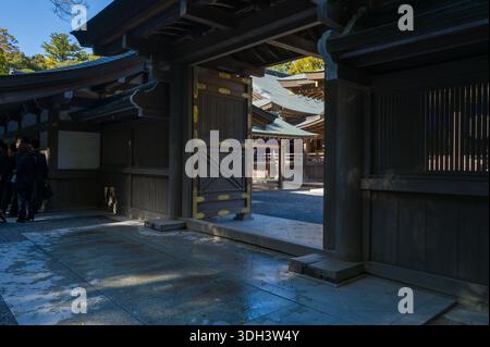 ISE, Japon - 29 octobre 2023 : une porte en bois avec des éléments décoratifs dorés s'ouvre sur la cour de la salle Kaguraden à ISE Jingu, avec plusieurs personnes debout dans la zone ombragée et l'architecture traditionnelle en bois visible à la lumière du soleil. Banque D'Images