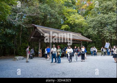 ISE, Japon - 29 octobre 2023 : des groupes de personnes se rassemblent et passent devant le pavillon de purification de temizuya en bois à Kotai Jingu, avec des arbres et du gravier visibles. Banque D'Images