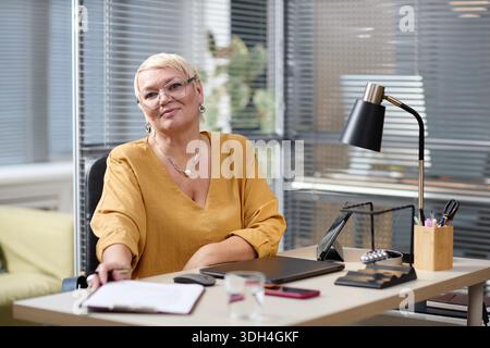 Portrait d'une femme caucasienne d'âge moyen souriant tout en étant assise au bureau Banque D'Images