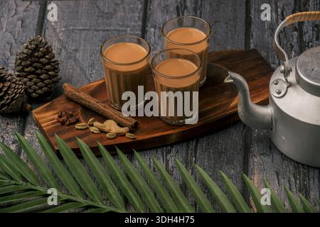 Un plateau en bois avec trois tasses de thé et une bouilloire est placé sur une table en bois. Le plateau est décoré de bâtonnets de cannelle et de gingembre, ce qui lui donne un Banque D'Images