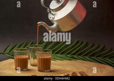 Le thé Masala est versé dans une tasse de chai de trois verres. Les tasses sont sur une table en bois. Coupe chai versé hors de la bouilloire à thé. Banque D'Images
