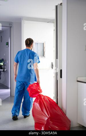 Une infirmière dédiée aux gommages bleus transporte les déchets médicaux dans une unité de soins intensifs hospitaliers. Le milieu moderne des soins de santé met en évidence leur rôle essentiel et leur engagement Banque D'Images