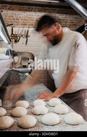 Un pizzeria expérimenté prépare avec diligence des boules de pâte sur un comptoir en granit dans une pizzeria animée, mettant en valeur l'art et la tradition de l'artisanat au Banque D'Images