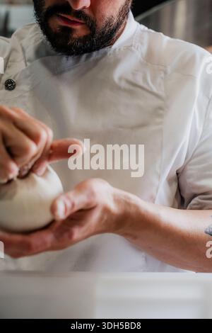 Un pizzeria qualifié fabrique habilement la pâte à la main dans une pizzeria traditionnelle. Le chef porte un uniforme blanc, travaillant avec la mise au point et la précision dans le Banque D'Images