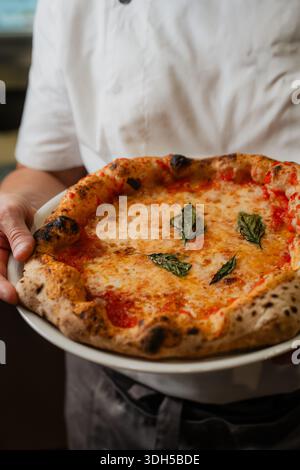 Un pizzeria qualifié présente une pizza napolitaine fraîchement cuite. La croûte dorée de pizza et les garnitures vibrantes mettent en valeur l'Italie traditionnelle Banque D'Images