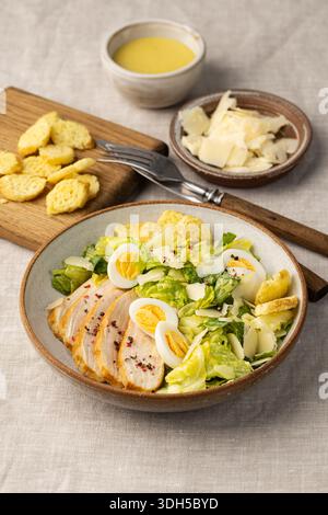 Une salade César avec iceberg et laitue romaine, poulet cuit au four, œufs de caille durs, copeaux de parmesan et croûtons, élégamment habillé en César d Banque D'Images