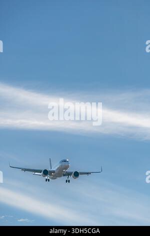 Un avion de passagers glisse en douceur à travers le ciel bleu clair, avec des nuages tortueux traînant derrière. La prise de vue grand angle capture l'impres de l'avion Banque D'Images