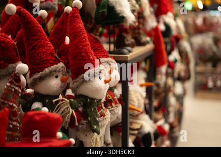 Jouets de bonhomme de neige festifs avec des chapeaux rouges en peluche et des foulards tricotés sont affichés sur des étagères en bois dans un magasin de jouets de Noël confortable, créant des vacances chaudes à Banque D'Images
