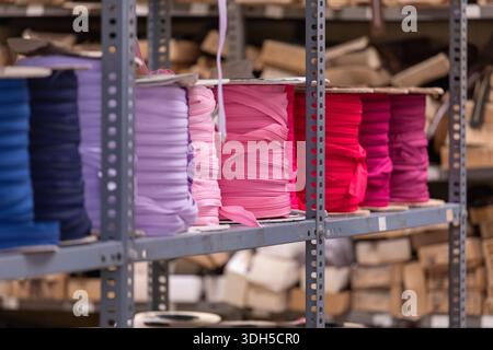 Des rouleaux de tissu empilés dans des tons vibrants de violet, rose et rouge sont soigneusement organisés sur des étagères en métal robustes dans un entrepôt, prêts à être utilisés dans divers Banque D'Images