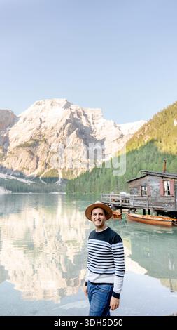 Une vue sereine au Lago di Braies dans les Dolomites, Italie. Un homme se tient au bord de l'eau, avec des bateaux en bois et des montagnes majestueuses reflétant dans le calme la Banque D'Images