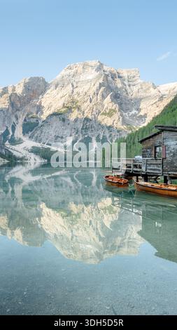 Vue panoramique sur le Lago di Braies dans les Dolomiti, Italie, avec des eaux cristallines reflétant les majestueux sommets montagneux. Des bateaux en bois et une cabane rustique ajoutent du charme Banque D'Images