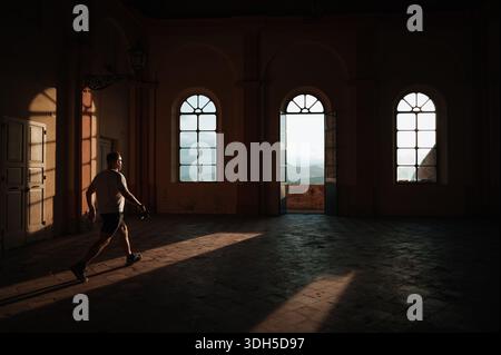 Dans un bâtiment italien historique, une personne se promène dans une pièce ensoleillée. Les ombres créent des motifs complexes sur le sol, ajoutant de la profondeur à la sérénité A. Banque D'Images