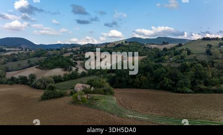 Vue drone sur les collines ondoyantes de l'Italie, avec une végétation luxuriante, de vastes champs ouverts et des montagnes lointaines sous un ciel bleu serein, capturant l'esse Banque D'Images
