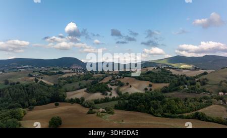 Vue aérienne de la pittoresque campagne italienne présentant des champs verdoyants, des collines ondulantes et des arbres dispersés sous un ciel bleu clair orné d'esprit Banque D'Images