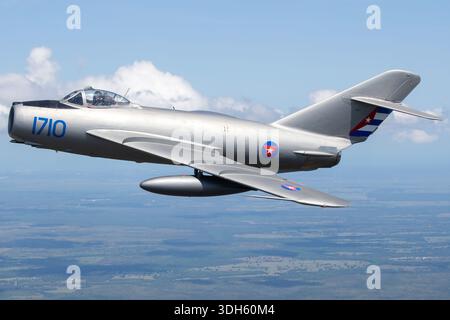 Cette image air-air documente un PZL-Mielec Lim-5, la forme polonaise du MiG-17F Mikoyan-Gurevich, qui vole pendant la Sun N Fun Aerospace Expo en Floride en 2025. Immatriculé N1710, l'avion porte des marques d'affichage de l'armée de l'air cubaine. Le Lim-5 est un chasseur monoplace équipé d'un turboréacteur Klimov VK-1F avec postcombustion. La photographie souligne la disposition de l'aile en flèche, l'entrée de nez et l'état général de la cellule de cet avion militaire préservé. Banque D'Images