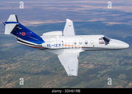 L'image présente le Cessna 525 CitationJet M2 immatriculé YU-SCM numéro de série 525-0918 en vol horizontal photographié depuis un avion à proximité. Le jet est propulsé par une paire de turboréacteurs Williams International FJ44-1AP-21 et sert de transport d'affaires léger moderne. Capturée lors du rassemblement aérien serbe Airpower 2025, la vue met en évidence la zone du cockpit, les lignes du fuselage et la structure de l'aile tandis que l'avion opère dans des conditions atmosphériques stables au-dessus de la Serbie avec un équipage professionnel à bord. Banque D'Images