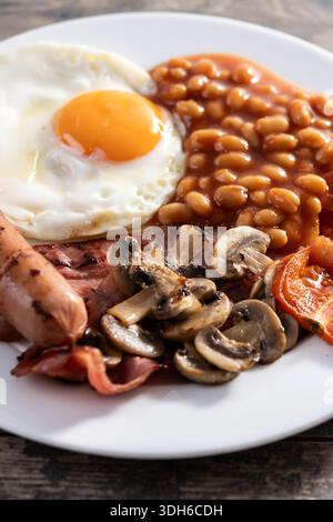 Petit déjeuner anglais complet avec oeuf frit, bacon, saucisses et haricots sur une table en bois Banque D'Images