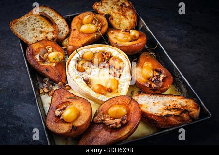 camembert cuit au four avec poires glacées caramélisées, noix et raisins et baguette servie sur une assiette en métal rustique Banque D'Images