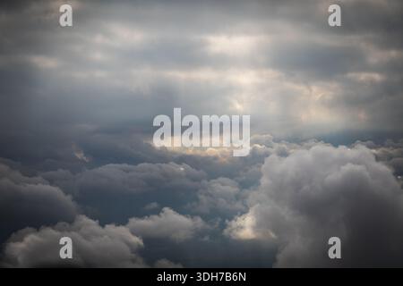 Une vue aérienne met en valeur un paysage nuageux spectaculaire sur la campagne suisse. Des rayons de soleil brillants traversent les nuages denses et gris, illuminant la secte Banque D'Images