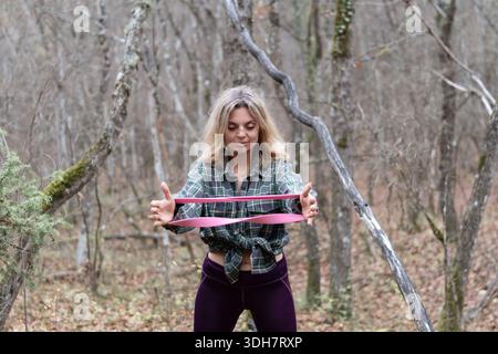 Femme exercice bande de résistance à l'extérieur dans le cadre boisé de forêt d'automne Banque D'Images