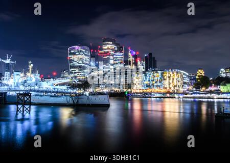 Vue nocturne sur les gratte-ciel de Londres avec des bâtiments modernes illuminés reflétant la Tamise. Banque D'Images