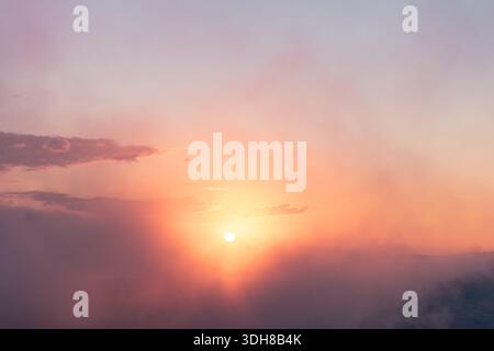 Un coucher de soleil doux et lumineux montrant un beau mélange de couleurs pastel dans le ciel. Le soleil brille brillamment derrière de minces nuages et un beau f Banque D'Images