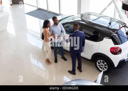 Concessionnaire automobile. Vue de dessus du couple de clients et du manager qui se mettent à la main après la transaction Banque D'Images