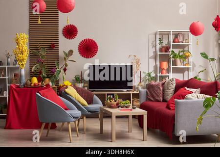 Salon décoré pour les vacances Tet avec des lanternes rouges, des ornements festifs, des plantes, des fruits et de la nourriture traditionnelle sur la table, des meubles modernes aménagés pour la célébration, pas de gens visibles Banque D'Images