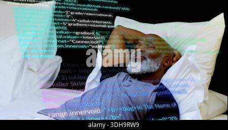 Homme senior inclinable portant un tee-shirt gris sur le lit avec des oreillers blancs, se reposant et regardant le code projeté Banque D'Images