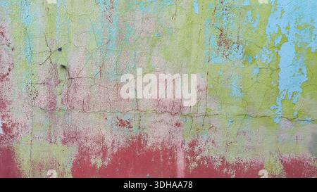 Gros plan d'un mur fortement altéré présentant des couches de peinture fissurée et écaillée dans les tons de vert, bleu et rouge. Banque D'Images